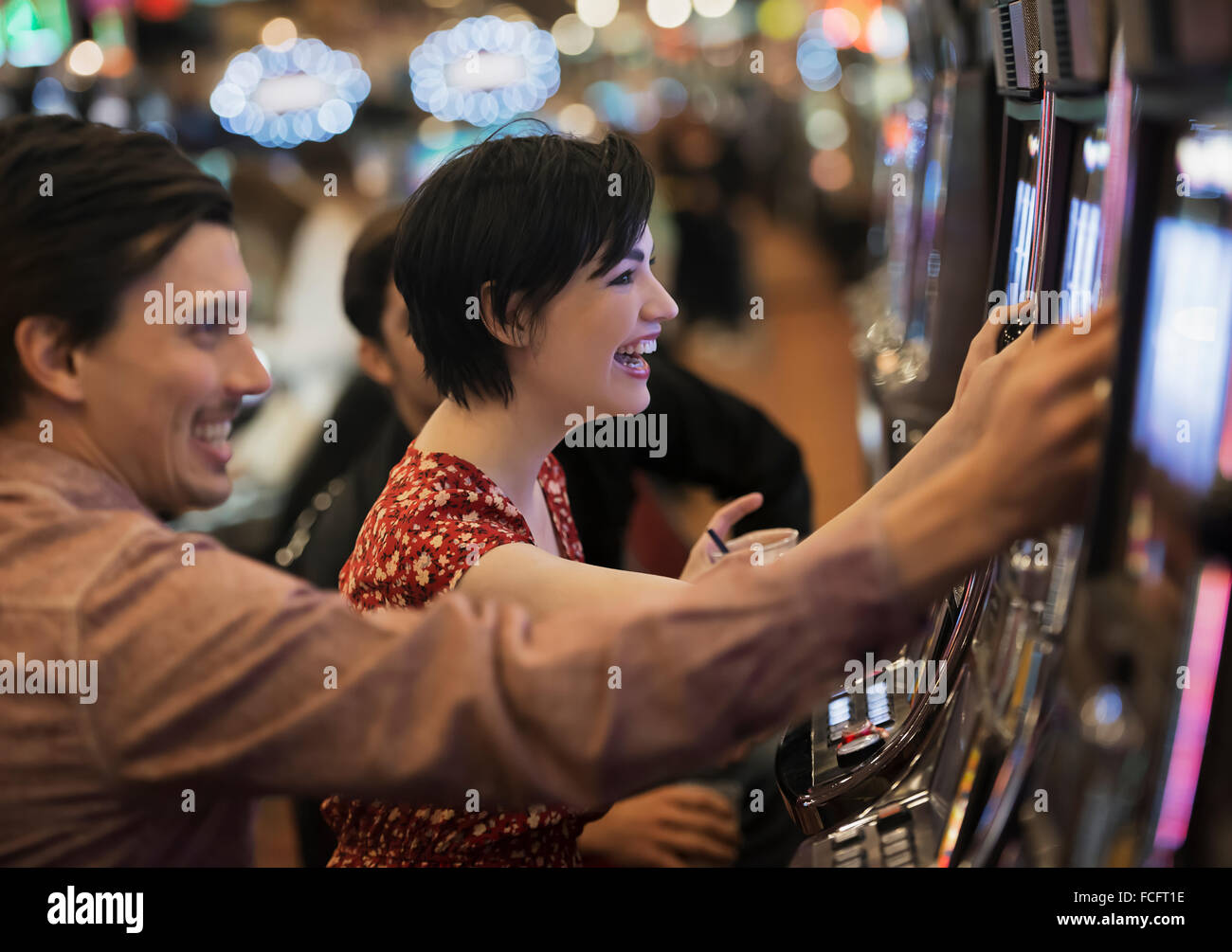 Zwei Personen, ein junger Mann und Frau, die Spielautomaten in einem Casino spielen. Stockfoto