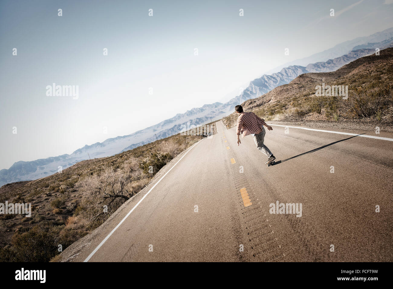 Ein junger Mann auf einer asphaltierten Straße in der Wüste auf einem Skateboard fahren. Stockfoto