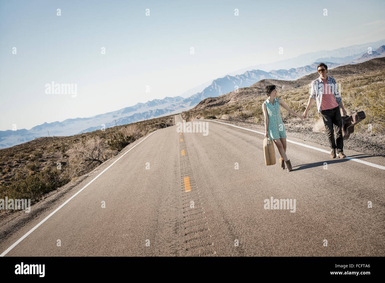 Ein junges Paar, Mann und Frau gehen hand in Hand auf eine asphaltierte Straße in der Wüste Tragetaschen. Stockfoto