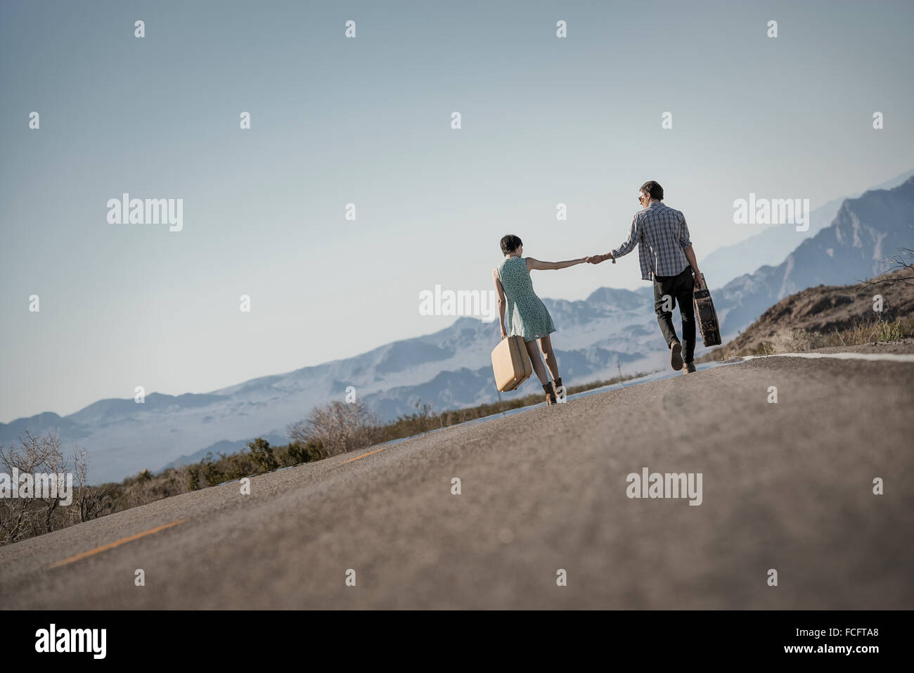 Ein junges Paar, Mann und Frau gehen hand in Hand auf eine asphaltierte Straße in der Wüste Tragetaschen. Stockfoto