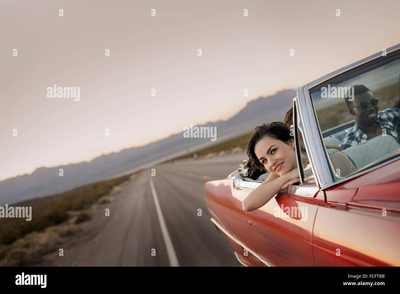 Eine Gruppe von Freunden in einem roten offenen oberen Cabrio Oldtimer auf einem Roadtrip. Stockfoto