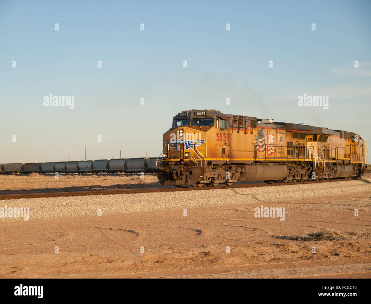 Gelber Zug mit amerikanischen Flagge unterwegs in einer Kurve vor einem blauen Himmel in der sandigen Wüste in Kalifornien, USA. Stockfoto