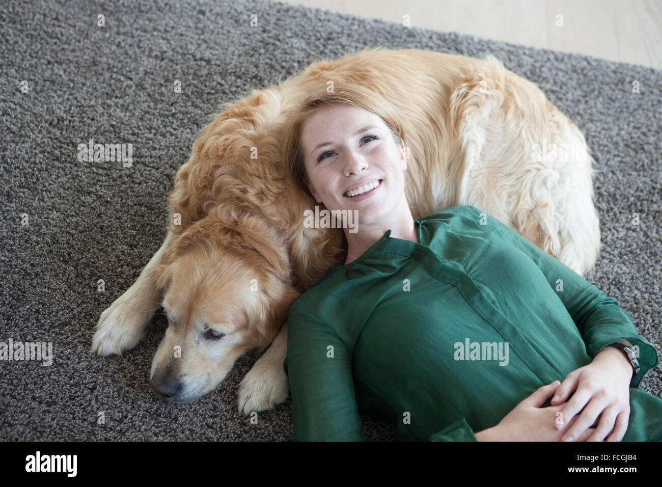 Lächelnde junge Frau entspannt ihren Hund auf dem Teppich Stockfoto