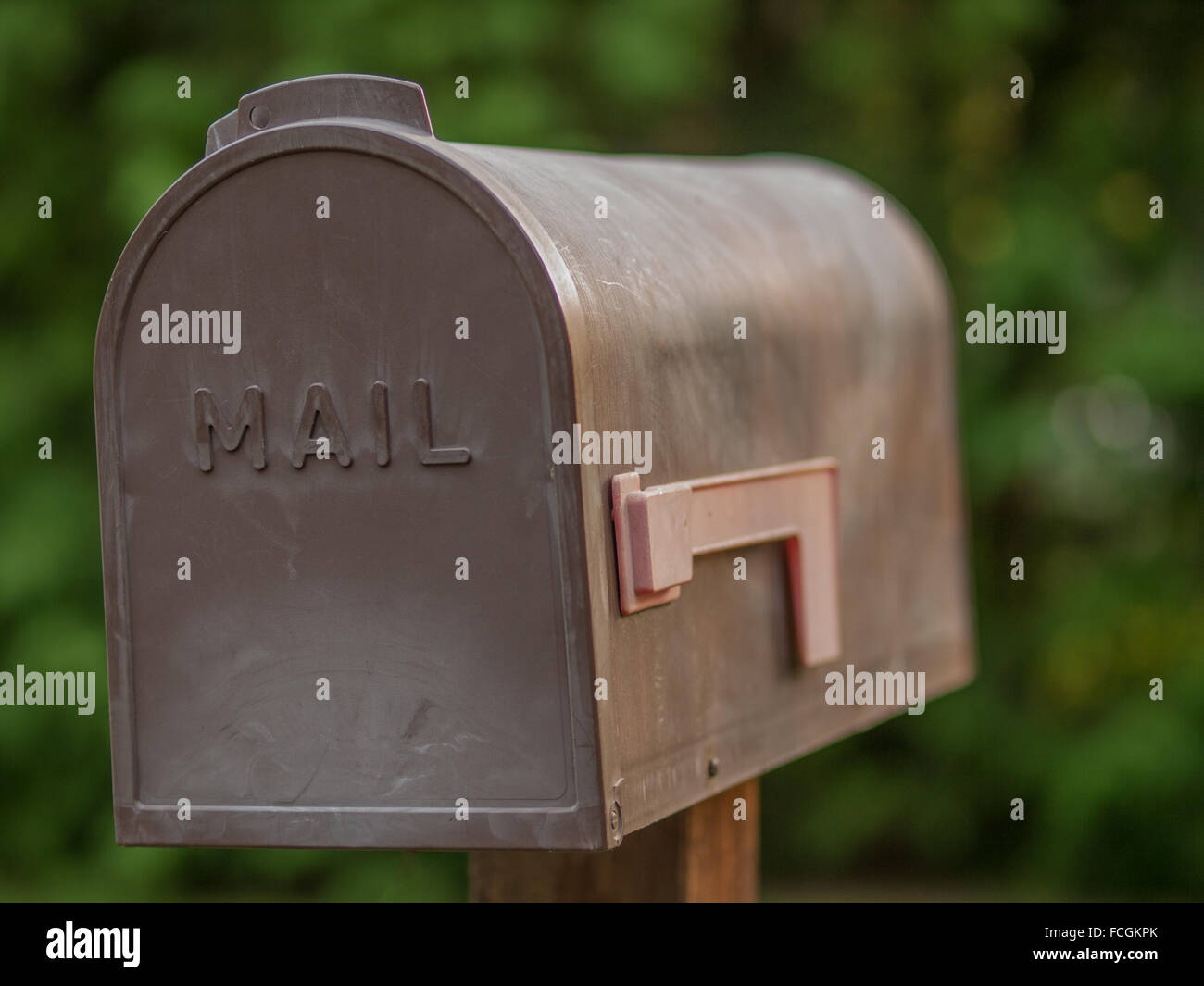 Braune Kunststoff Postfach mit dem Wort Post eingeschrieben drauf, eine rote Fahne, das ausfällt, vor grünem Hintergrund unscharf, auf eine w Stockfoto