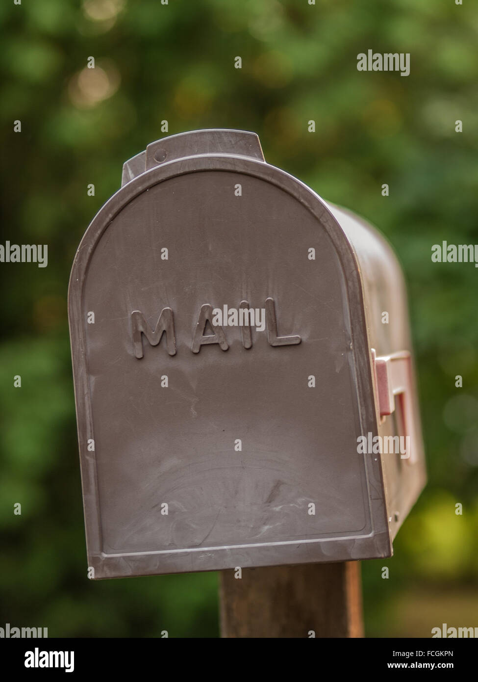 Braune Kunststoff Postfach mit dem Wort Post eingeschrieben drauf, eine rote Fahne, das ausfällt, vor grünem Hintergrund unscharf, auf eine w Stockfoto