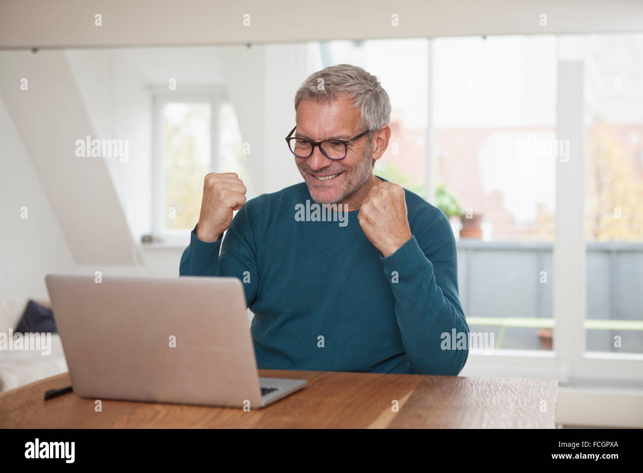 Reifer Mann zu Hause betrachten Laptop jubeln Stockfoto