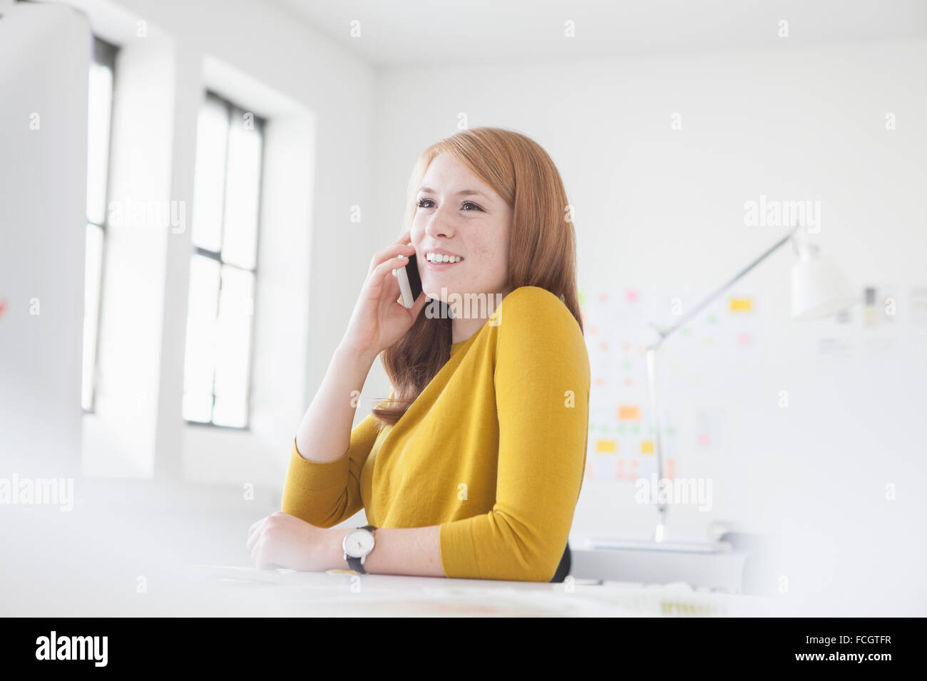 Junge Frau im Büro am Schreibtisch mit Smartphone Stockfoto