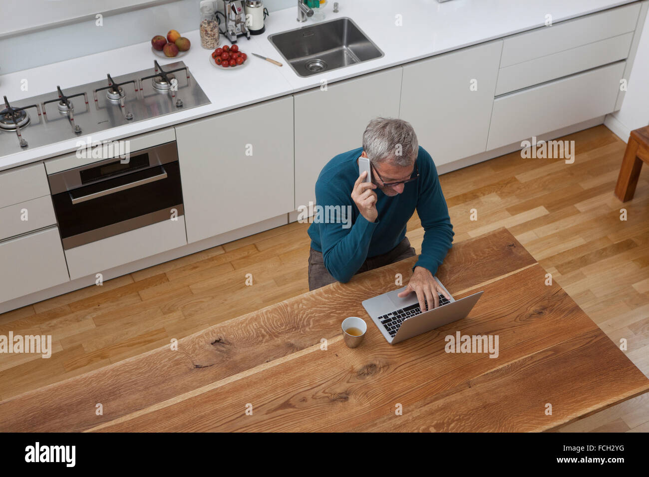 Reifer Mann in der Küche-Handy und laptop Stockfoto