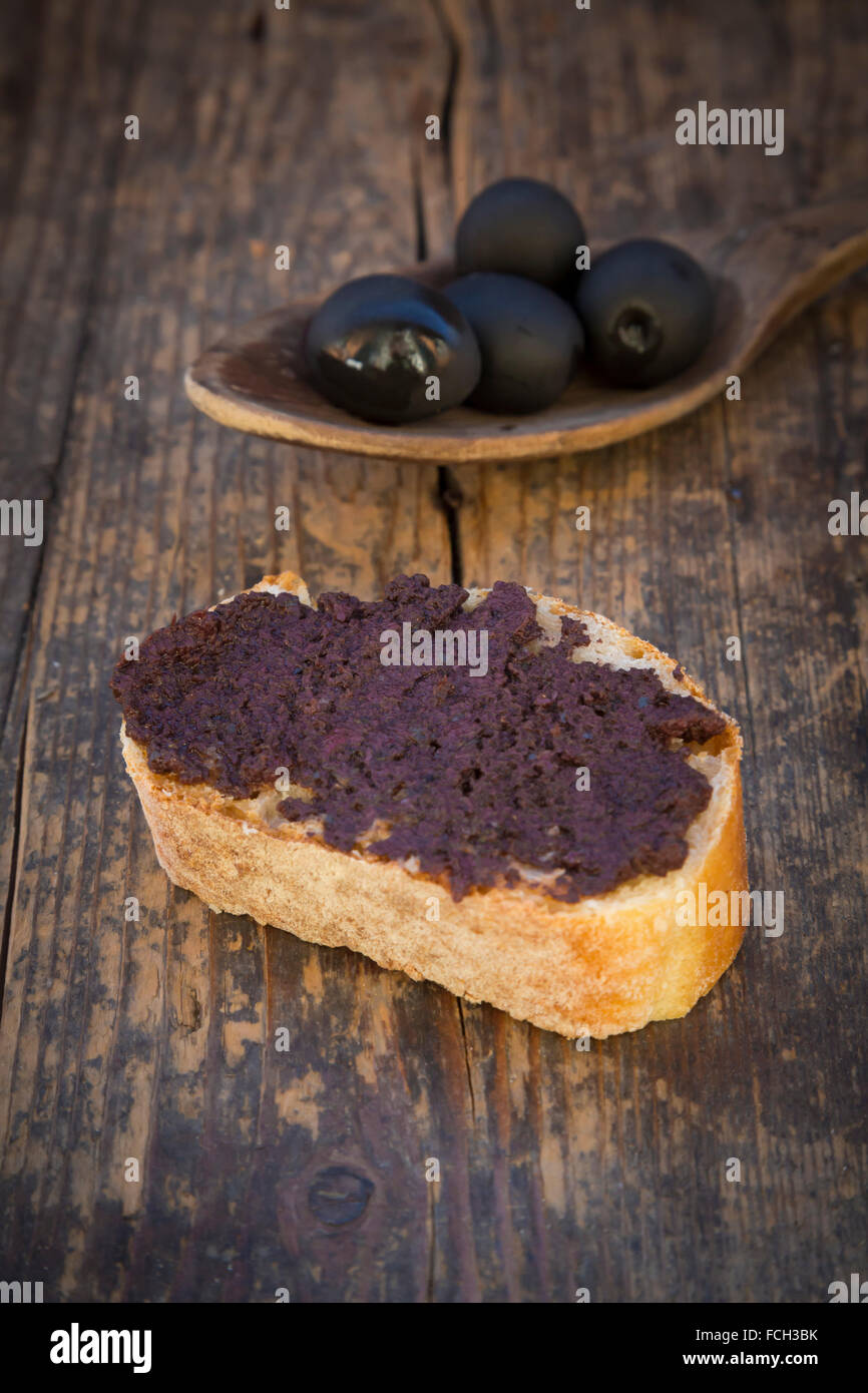 Holzlöffel aus schwarzen Oliven und Scheibe Weißbrot Oliven-paste Stockfoto