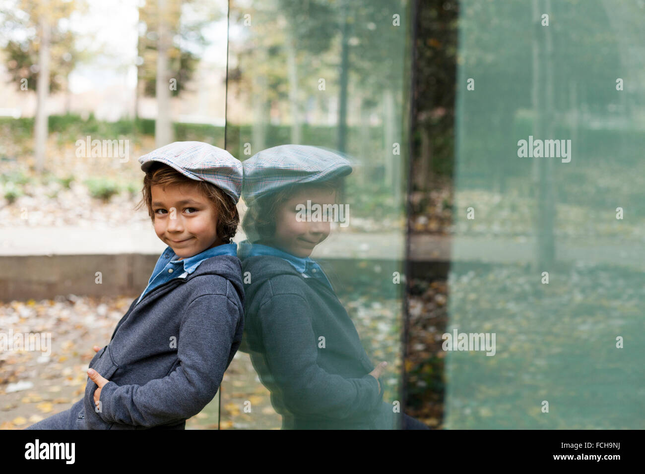 Porträt von lächelnden kleinen Jungen und seinem Spiegelbild auf eine Glasscheibe Stockfoto