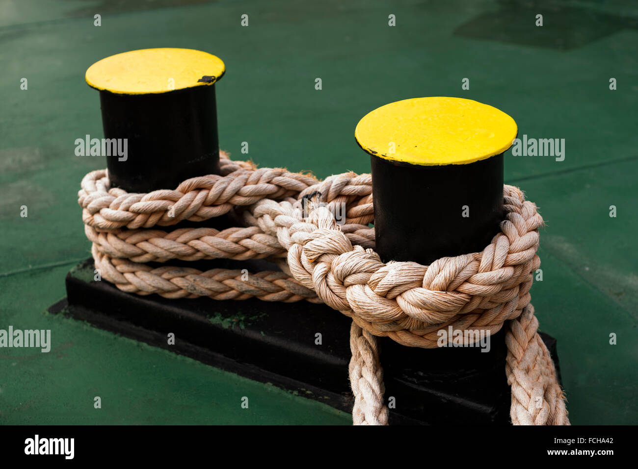 Gelben Poller verbunden mit einem Seil auf einem grünen Deck auf einem Schiff. Stockfoto