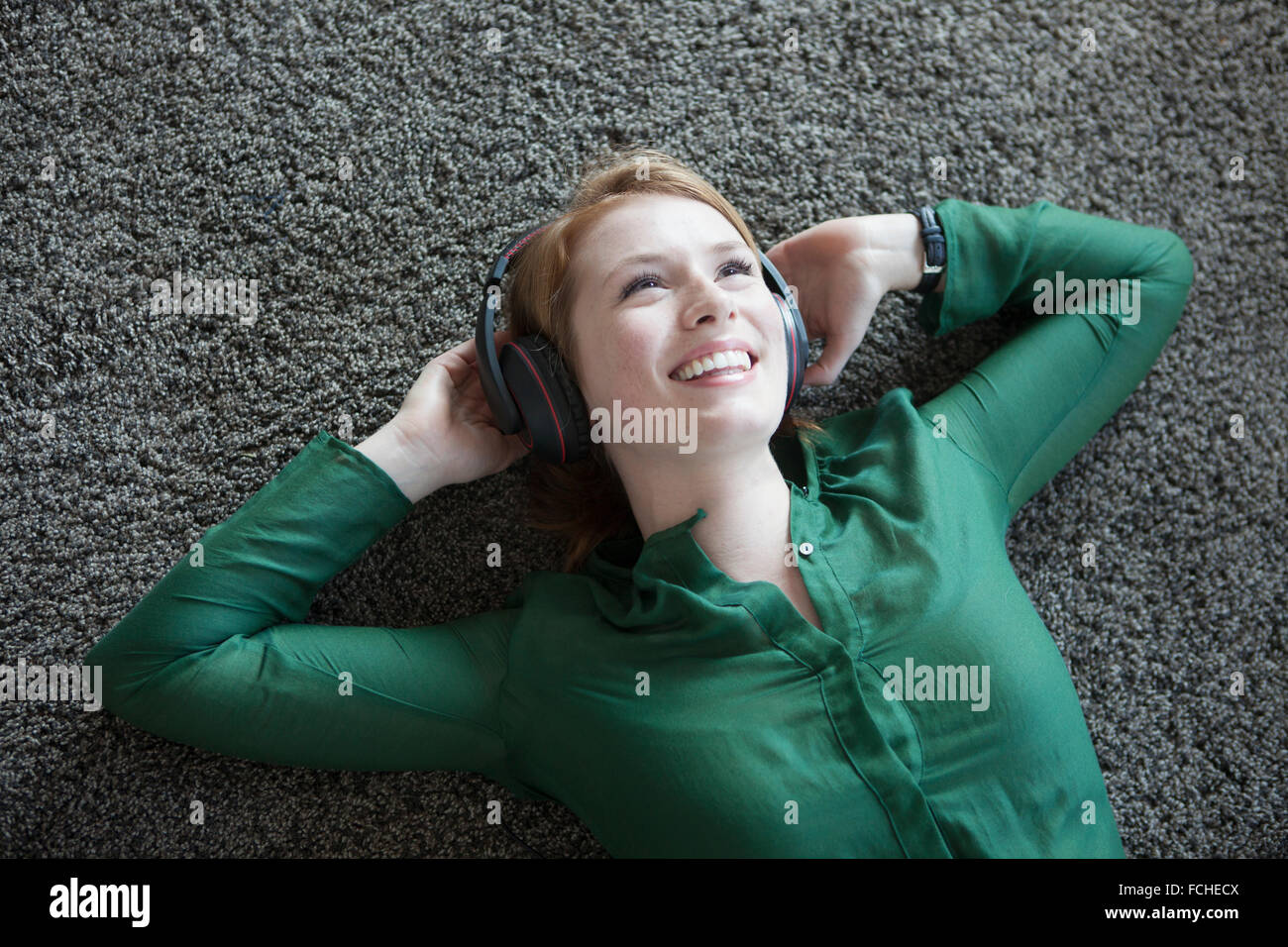 Lächelnde junge Frau liegend auf Teppich hören Musik Kopfhörer Stockfoto