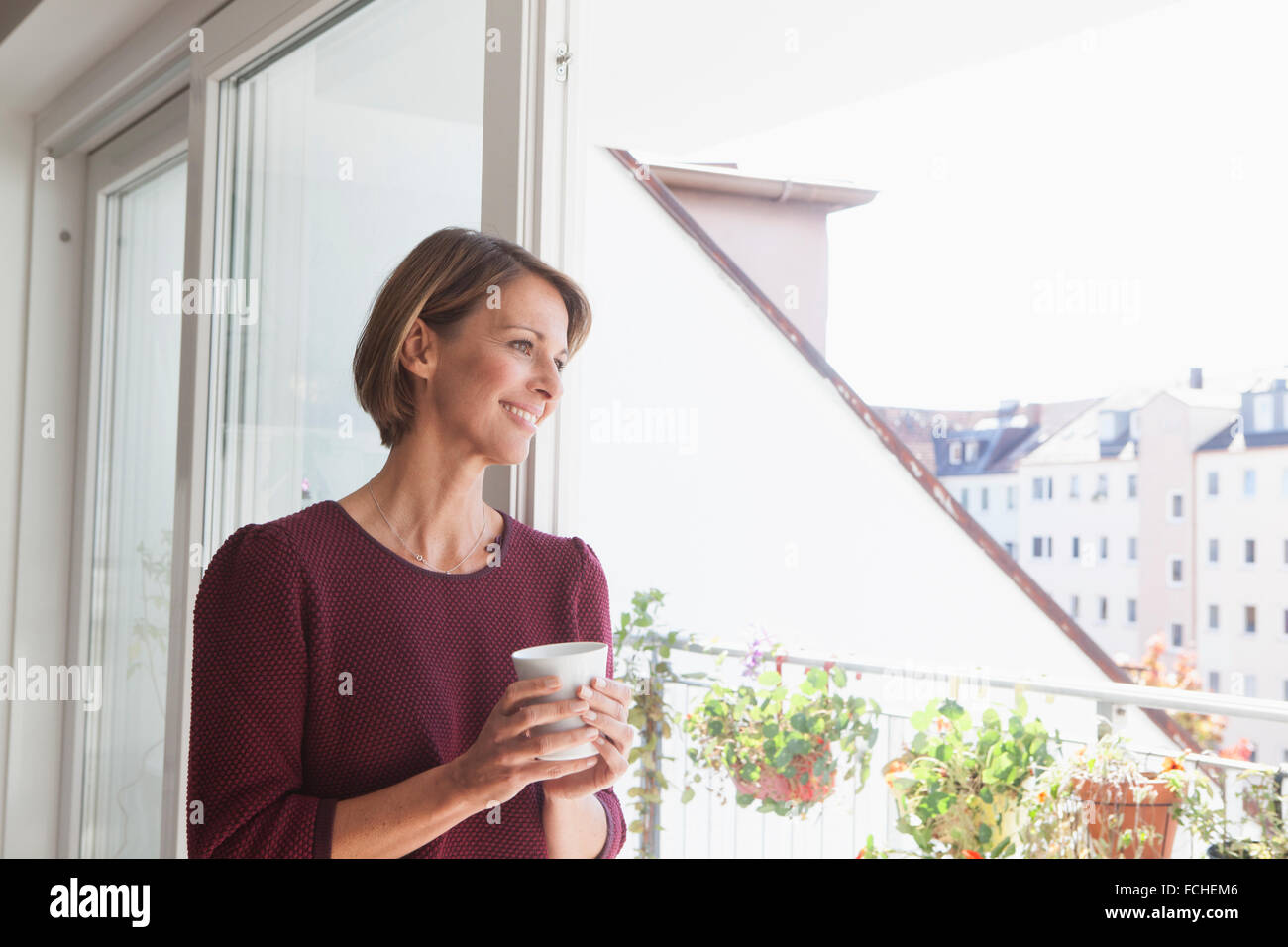 Lächelnde Frau gelehnt Balkontür man Entfernung Stockfoto