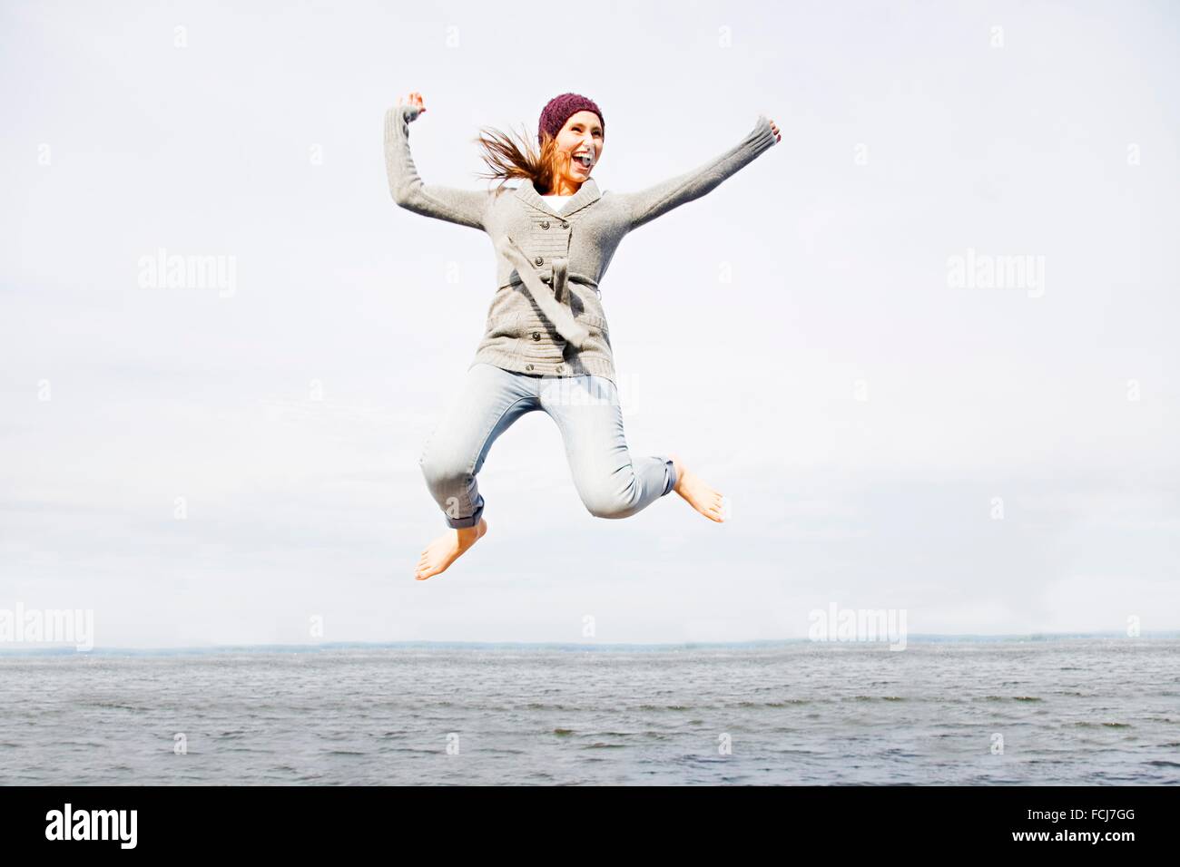 Junge Frau strahlend vor Glück springen am Meer Stockfoto