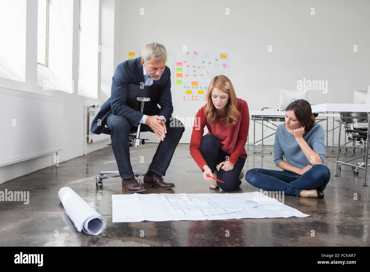 Geschäftsmann und zwei Frauen im Büro betrachten Bauplan Stockfoto