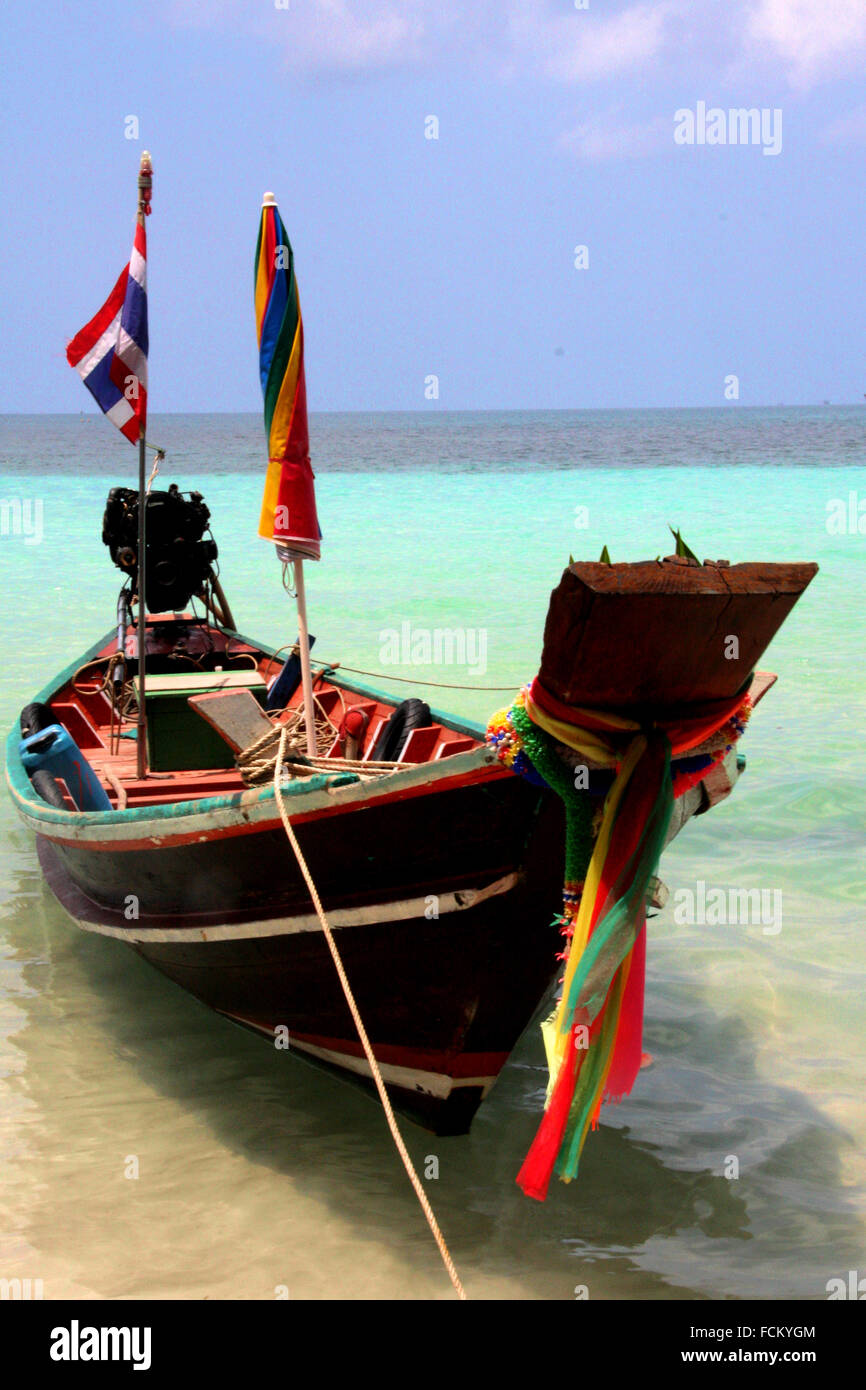 Ein langes Boot verankert an der Küste von Thailand, mit bunten Fahnen geschmückt. Weißer Sand, blaues Wasser in einer ruhigen Umgebung. Stockfoto