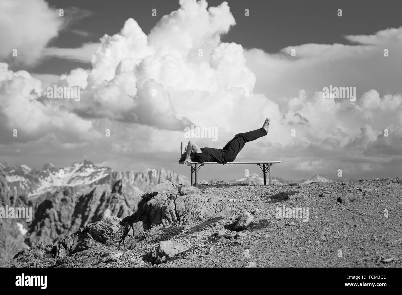 Der Mensch trainiert auf einer Bank in den österreichischen Bergen vor sommerlichen Cumuluswolken, Klippen und Felsen Stockfoto