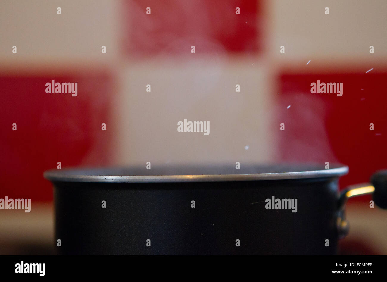Pfanne mit kochendem Wasser dämpfen vor roten und weißen Küchenfliesen Stockfoto