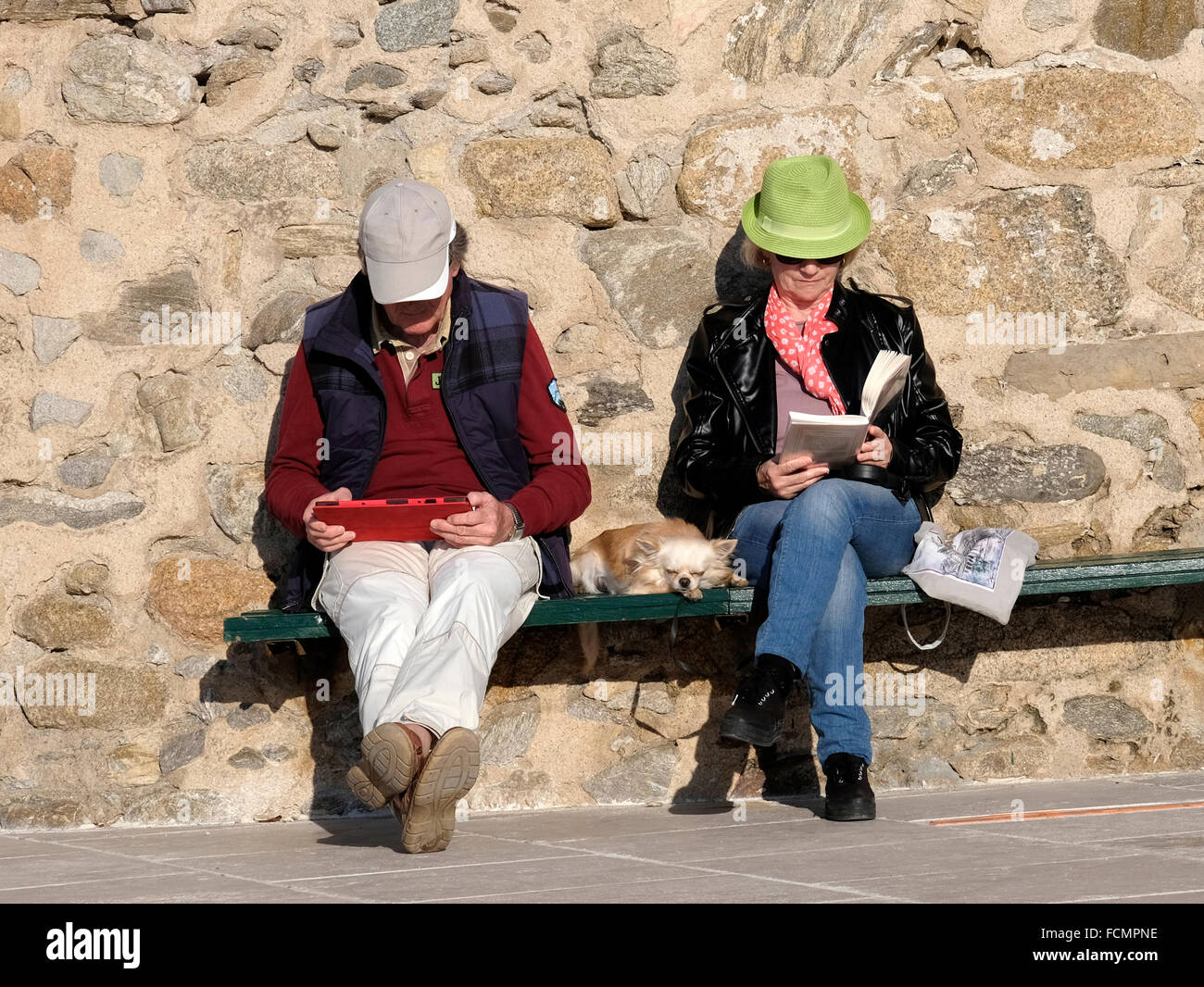Applying paar im Urlaub in St. Tropez, beide sitzen, eine von einem Tablet, eine aus einem Buch lesen.  Kleiner Hund zwischen ihnen. Stockfoto