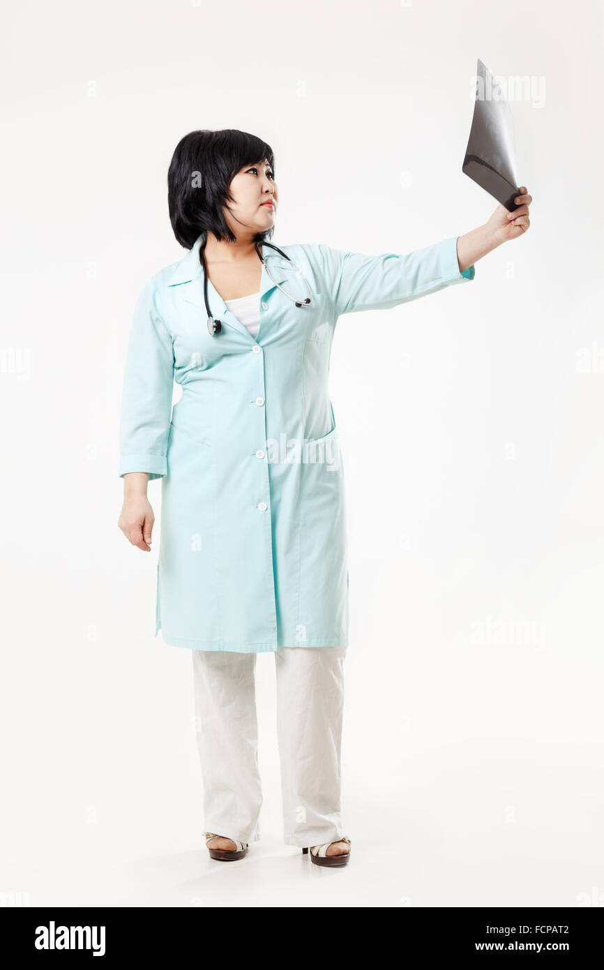 Kurvige Frau Doktor Stand hält die Ergebnisse der Radiologie, Röntgen Schädel Bild ausgestreckten Arm, in Türkis medizinische Kleid mit Stethoskop. Asiatischen aussehen, dunkle kurze Haare. Stockfoto