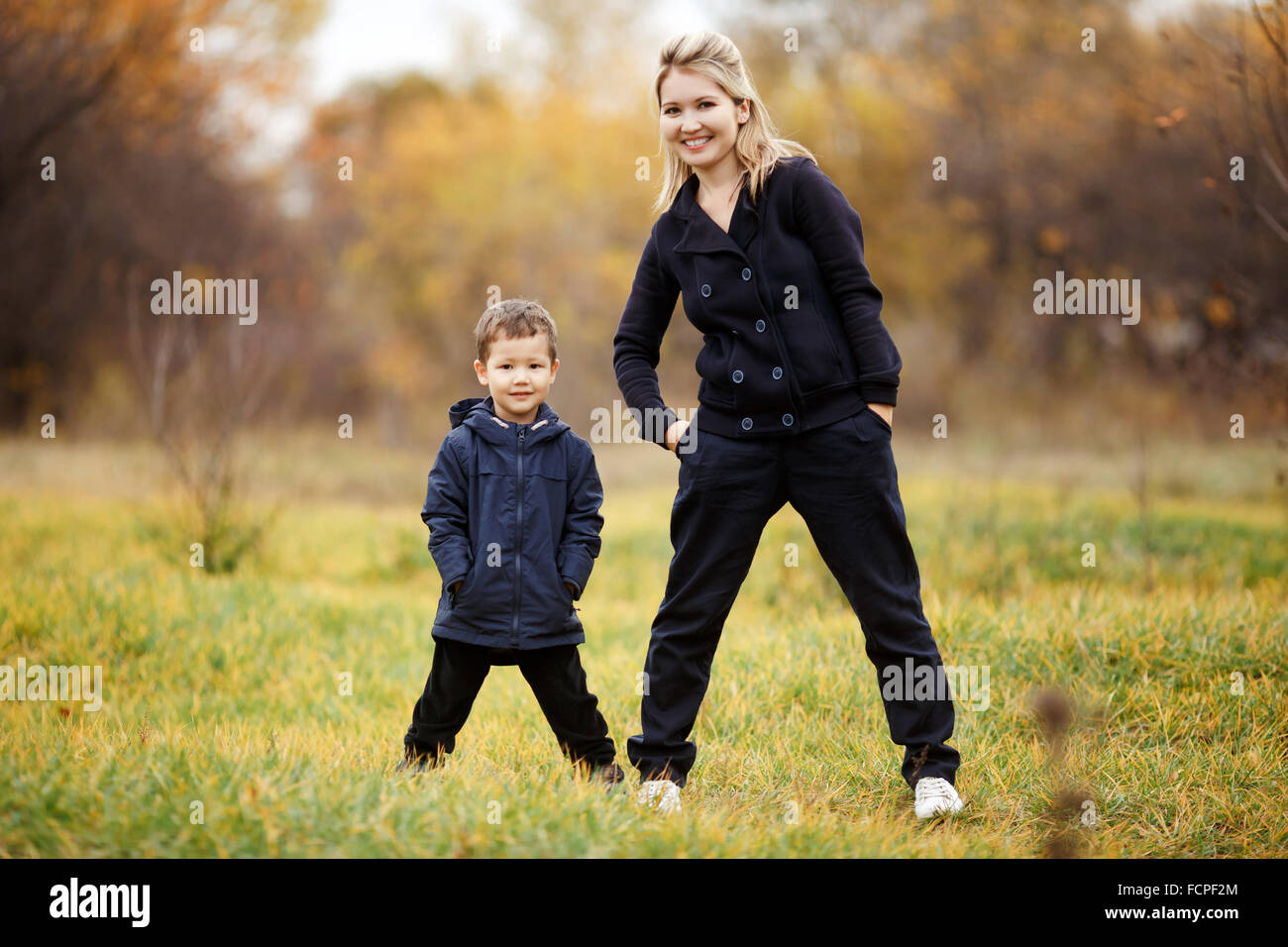Junge Mutter und Sohn im Waldpark, gelbes Herbstlaub. Freizeitkleidung. Kinder tragen blaue Jacke. Unvollständige Familie, posieren, Blick in die Kamera positiv. Kindheit, Kinder, deren Eltern sind die besten Freunde. Stockfoto