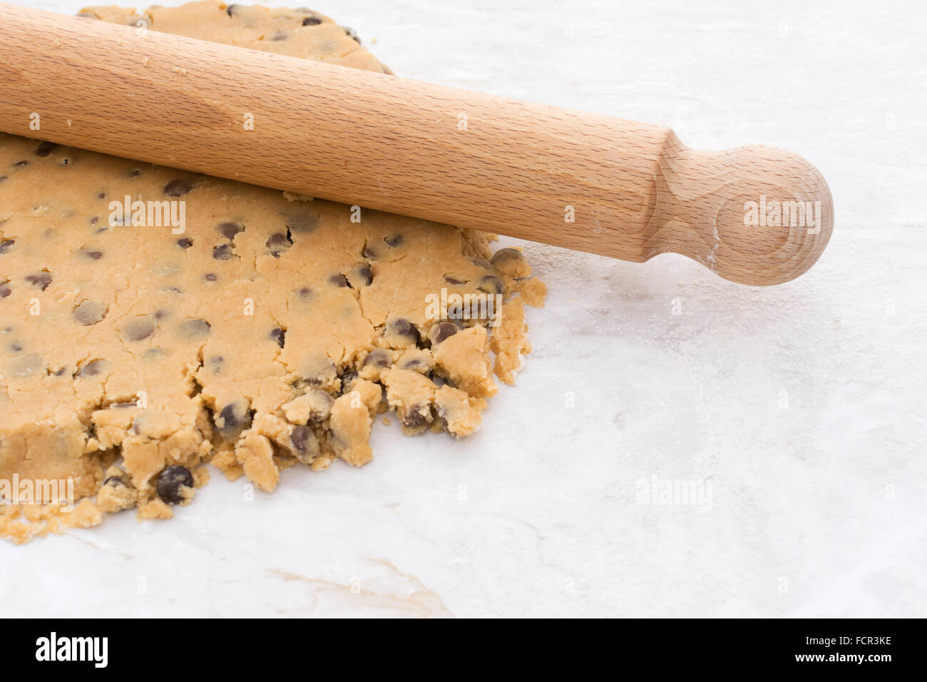 Hölzernen Nudelholz verwendet wird, um Schokolade Chip Shortbread Cookie-Teig auf einer bemehlten Arbeitsfläche ausrollen Stockfoto