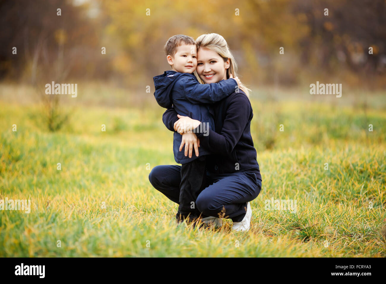 Junge Mutter und Sohn im Waldpark, gelbes Herbstlaub. Freizeitkleidung. Kinder tragen blaue Jacke. Unvollständige Familie, posieren, Blick in die Kamera positiv. Kindheit, Kinder, deren Eltern sind die besten Freunde. Stockfoto