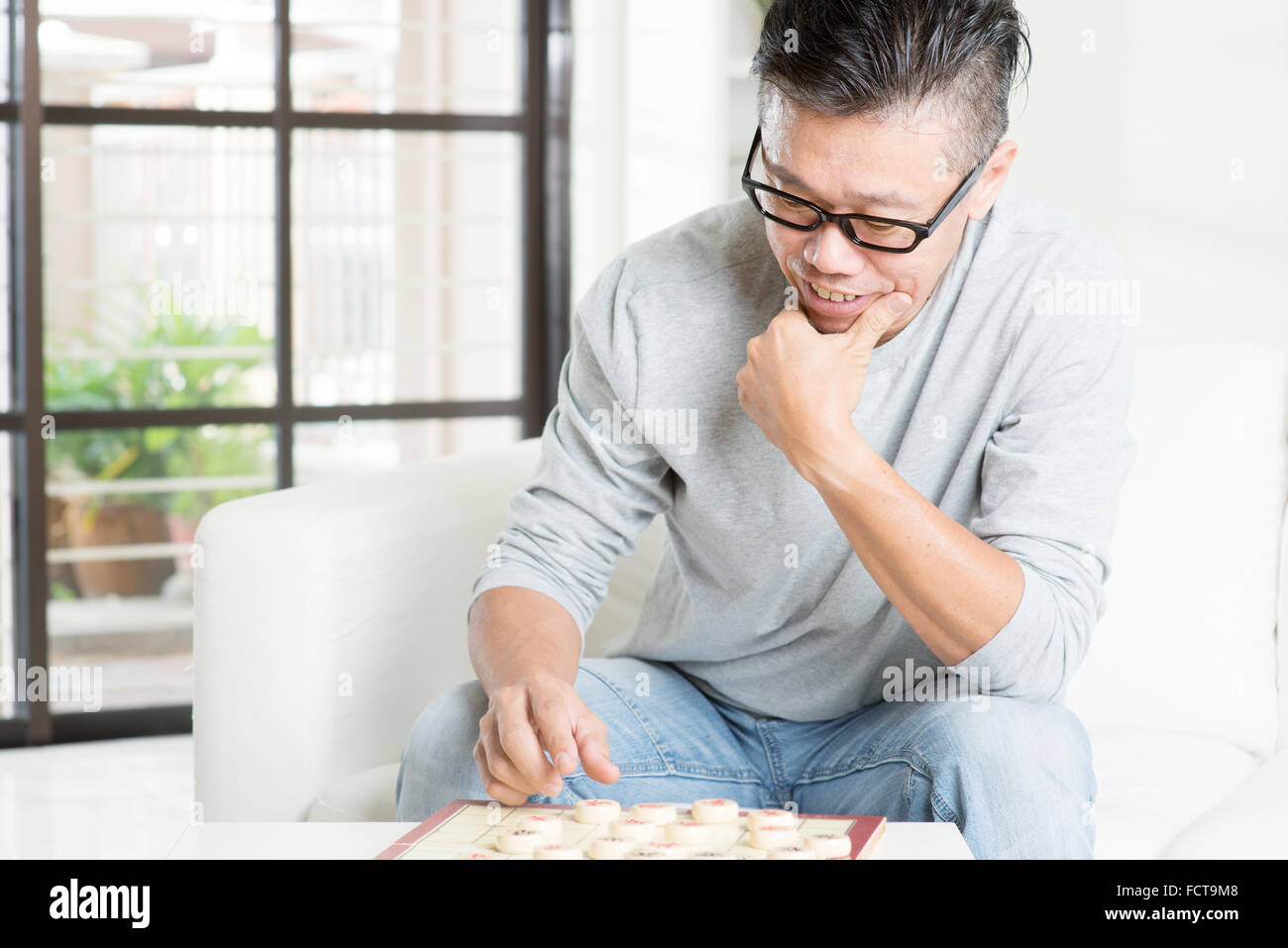 Reife 50er Jahre asiatischen Mann spielen China-Schach, sitzen auf der Couch zu Hause. Stockfoto