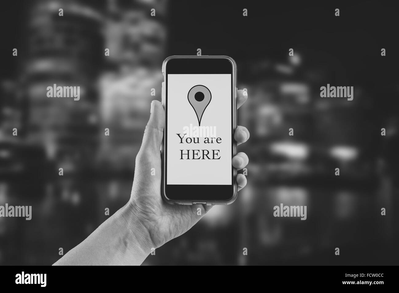 Weibliche Hand hält ein Mobiltelefon vertikal mit "Sie befinden sich hier" Text und Ortsmarke auf dem Bildschirm. Auf der städtischen Hintergrund jedoch unscharf Stockfoto