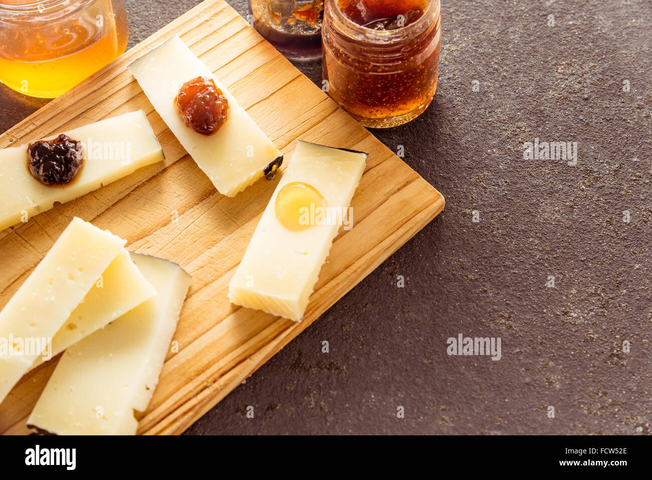 Eine Komposition aus italienischen Pecorino Käsescheiben mit Marmeladen von verschiedenen Geschmacksrichtungen auf ein Schneidbrett aus Holz Stockfoto