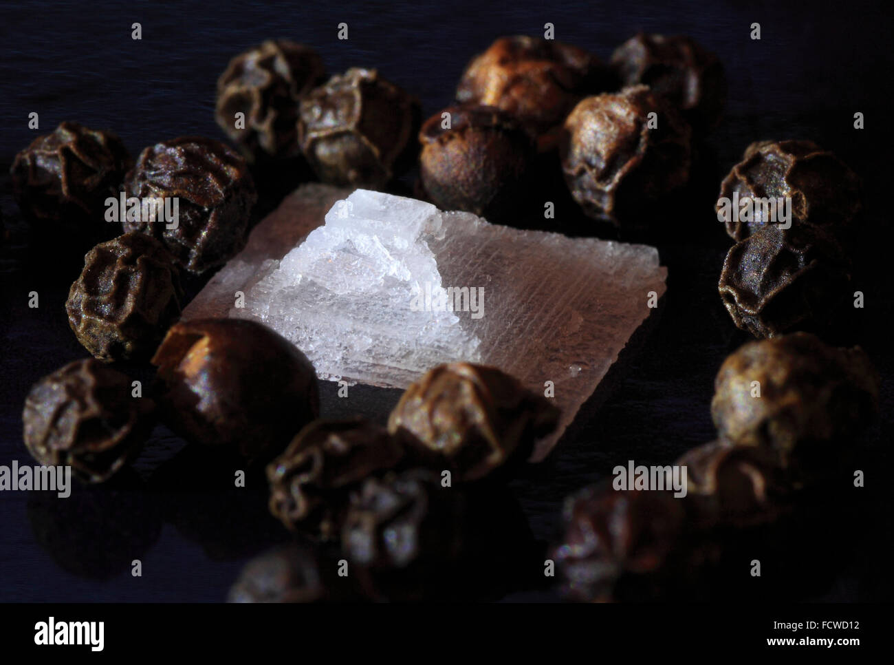 Meer-Salz-Kristall und ganze schwarze Pfefferkörner auf einem schwarzen Hintergrund. Stockfoto