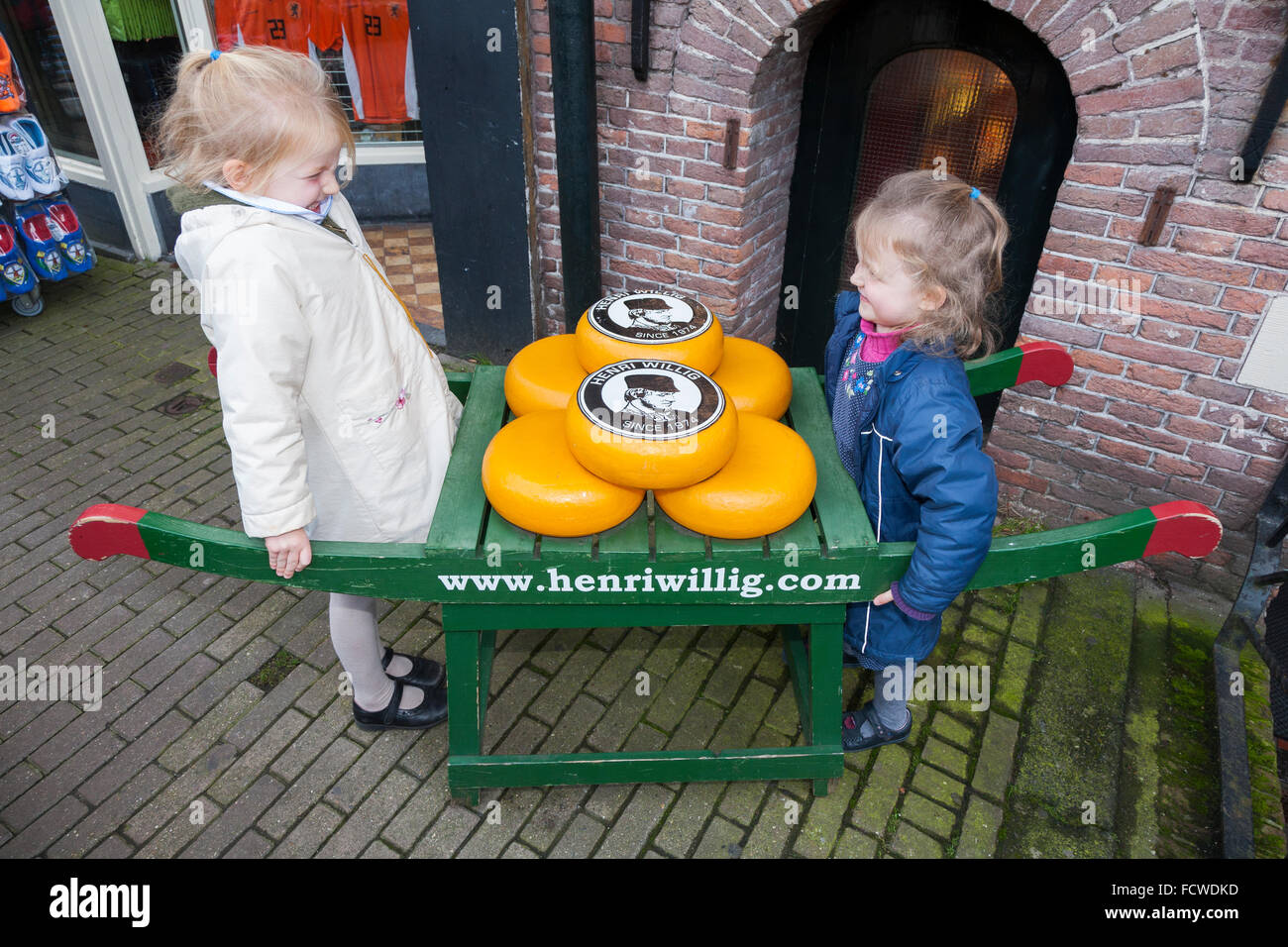 Kinder und Anzeige der Gouda-Käse auf einer traditionellen hölzernen Karren vor Henri Willig Shop, Amsterdam Holland Niederlande Stockfoto