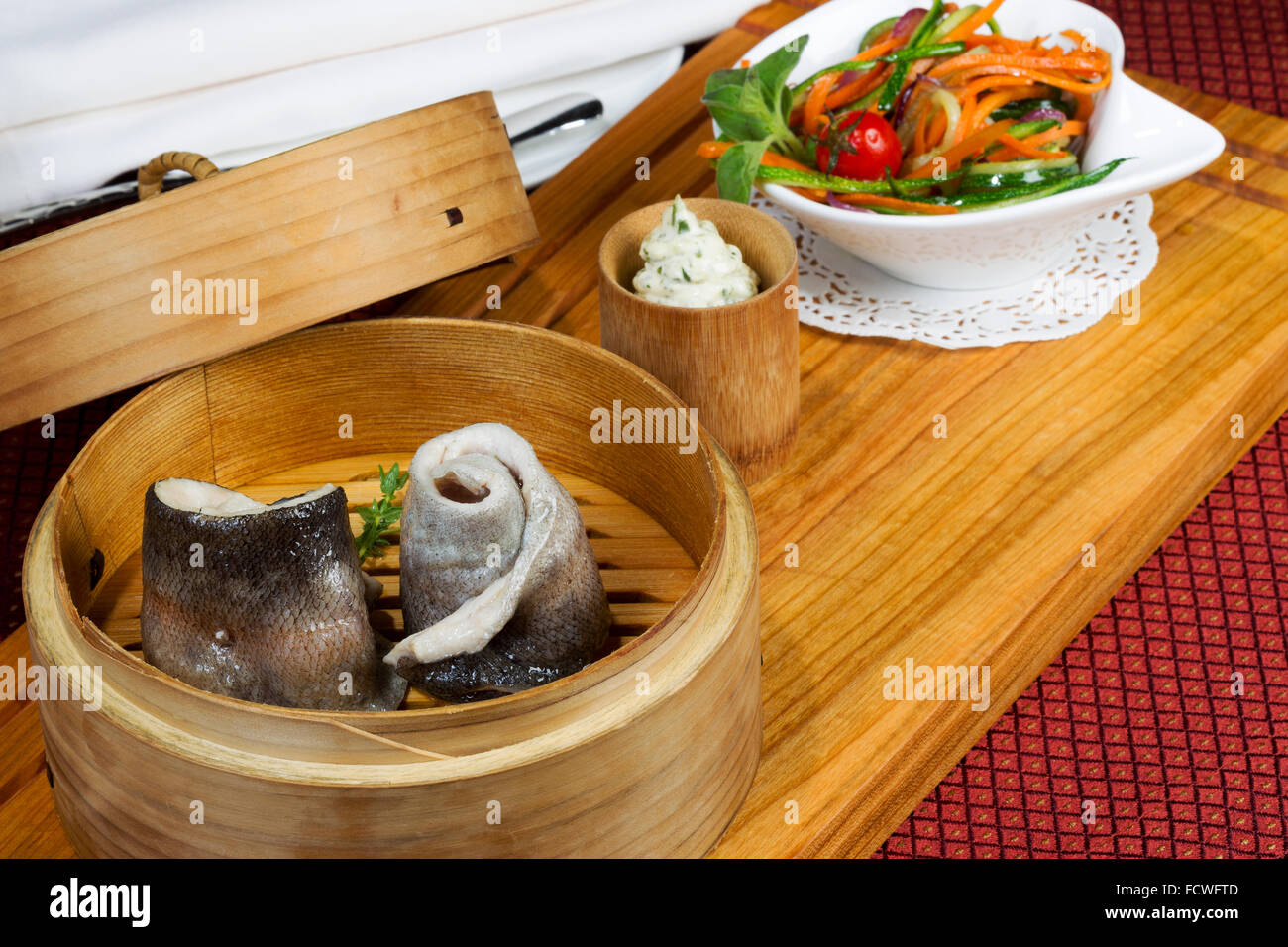Geschirr, Holz Cup mit gedünstetem Fisch, Salat, Besteck. Kreative Küche. Stockfoto