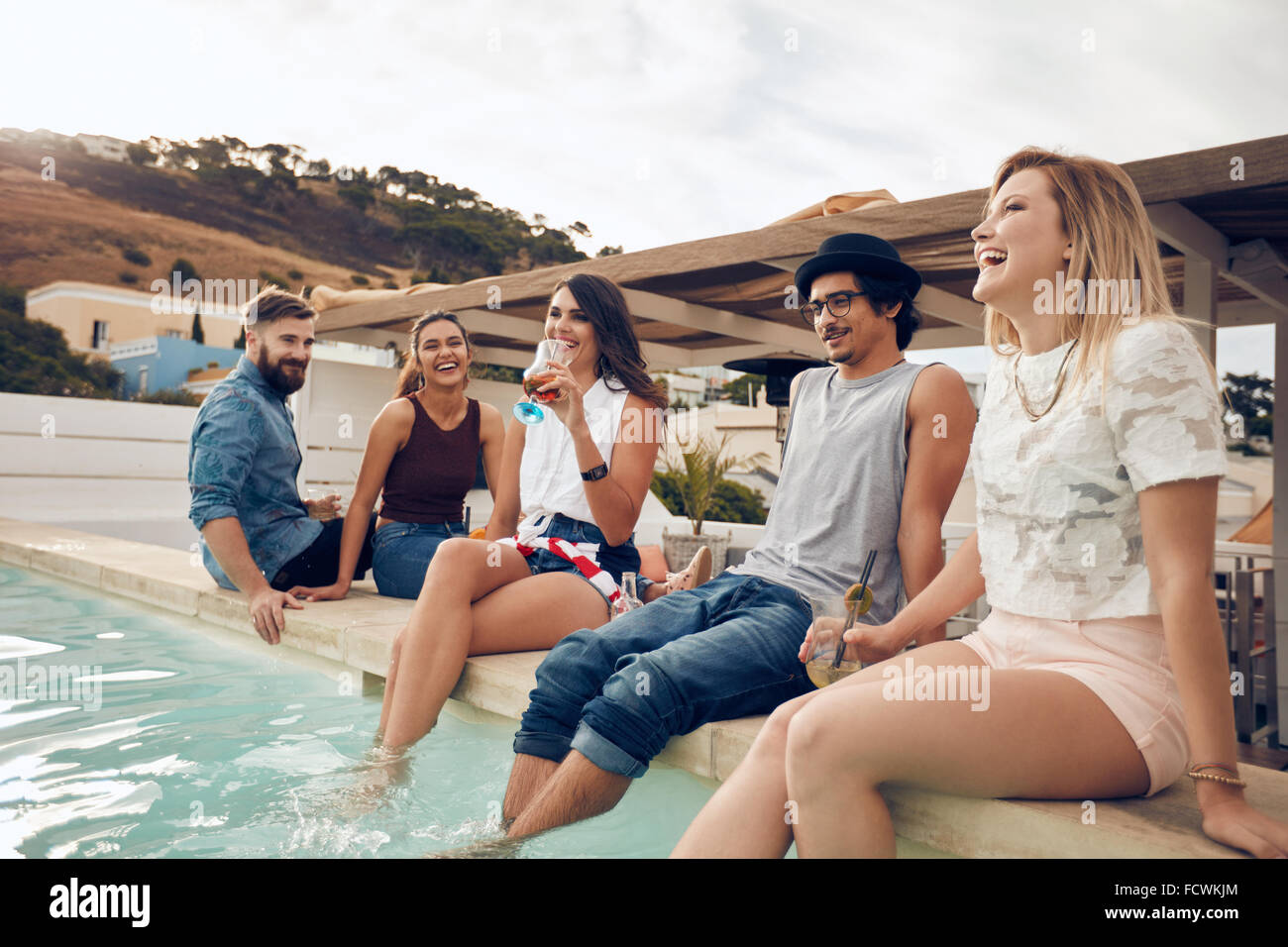 Junge Leute trinken Cocktails am Pool während der Partei. Junge Freunde lachen während der Sitzung von einem Schwimmbad. Männer und Frauen Stockfoto