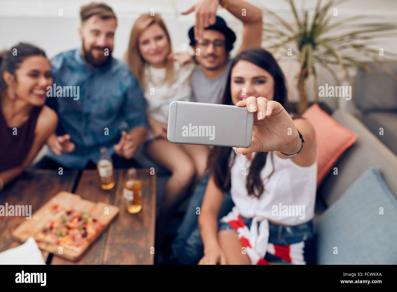 Junge Freunde in einer Partei unter Selbstbildnis mit Smartphone. Konzentrieren Sie sich auf Handy in Frauenhand. Gruppe von Jugendlichen sitzen Stockfoto