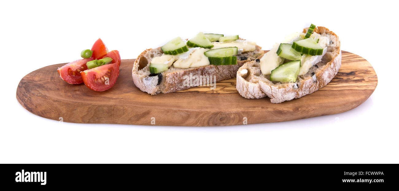 Gurke und Brie Sandwich auf Olivenöl Brot mit Tomaten und Frühlingszwiebeln auf einem Olivenholz Servierplatte über einem weißen Hintergrund Stockfoto