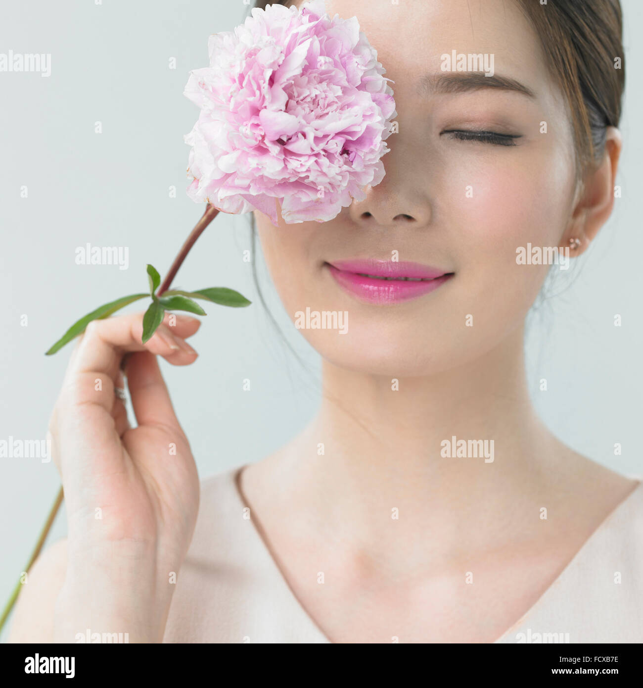 Frau, die eine Blume ihr Auge abdecken und lächelnd mit den Augen geschlossen Stockfoto