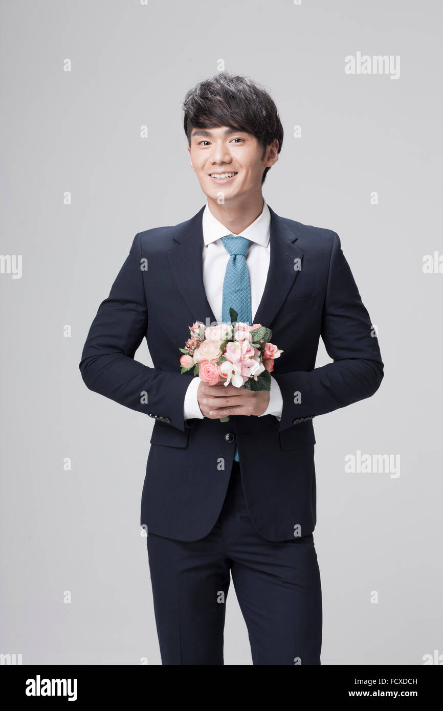 Mann im schwarzen Anzug und blaue Krawatte Blumen in der Hand hält und lächelnd Stockfoto