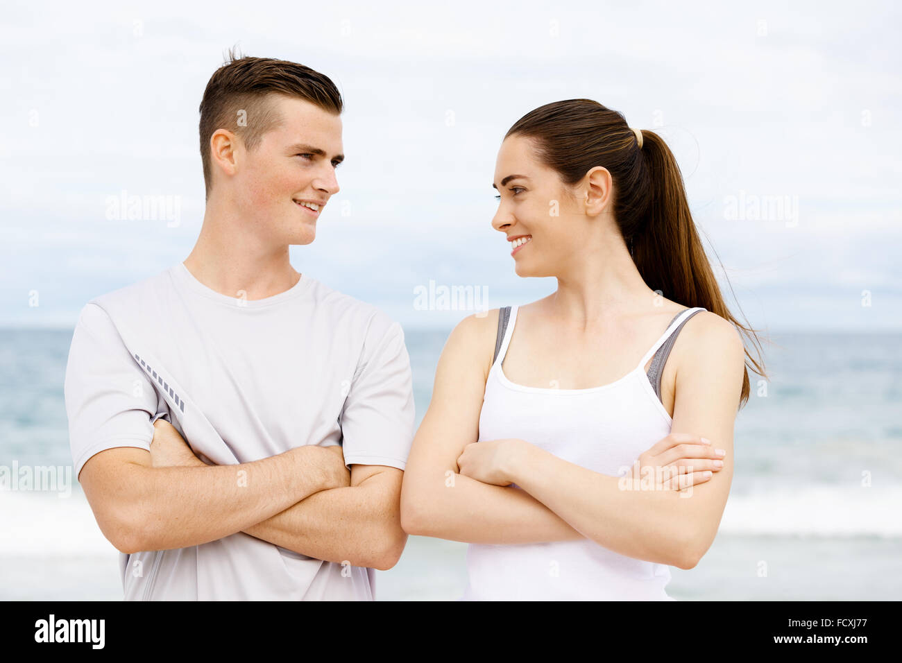 Junges Paar sahen einander stehend am Strand in Sportbekleidung Stockfoto