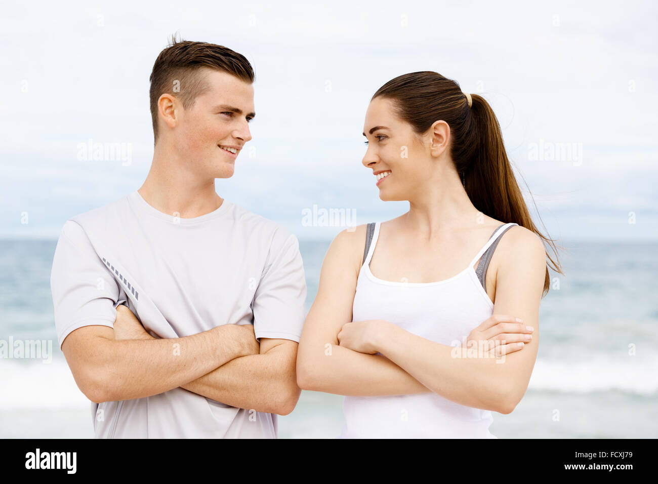 Junges Paar sahen einander stehend am Strand in Sportbekleidung Stockfoto