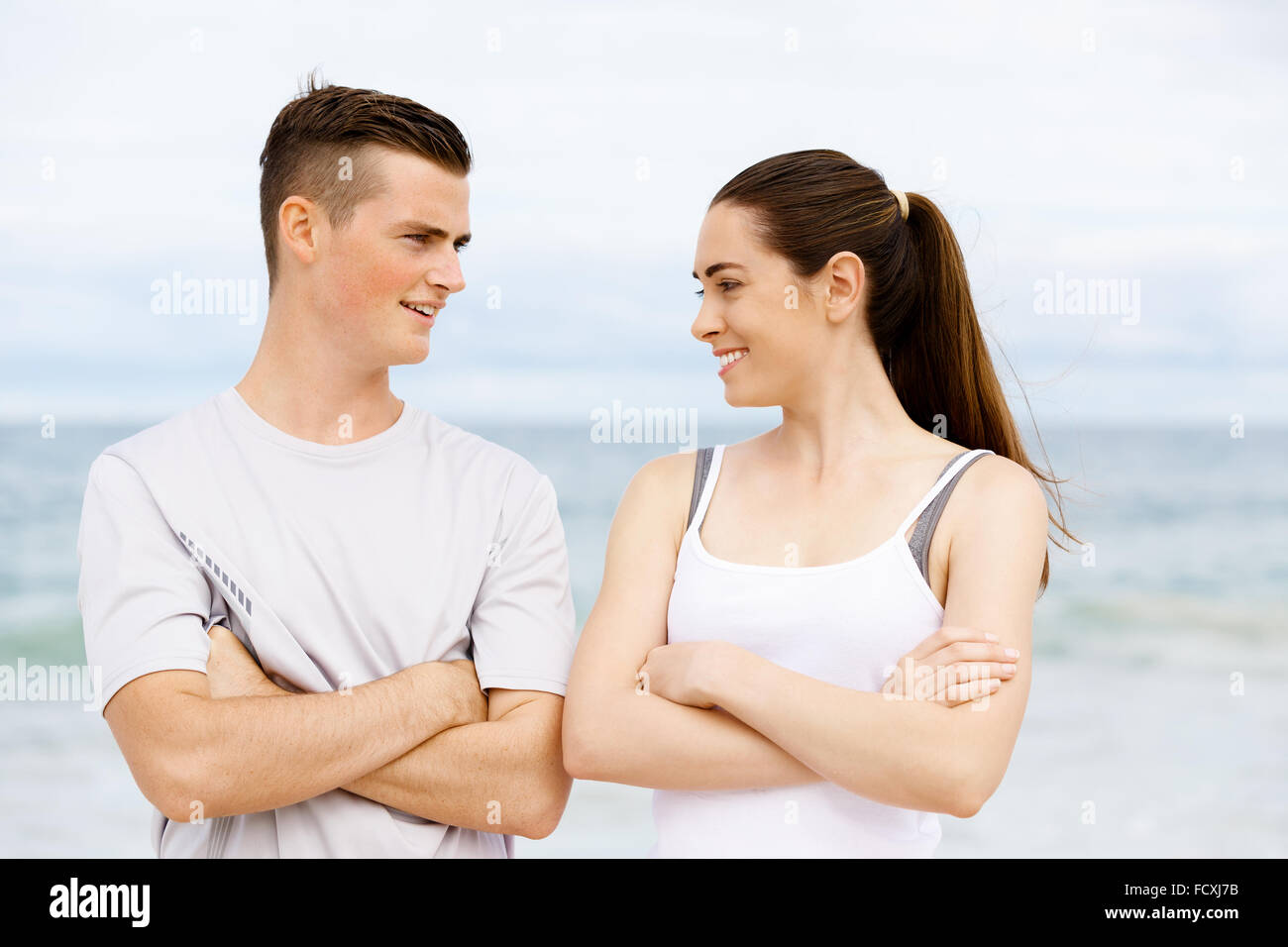 Junges Paar sahen einander stehend am Strand in Sportbekleidung Stockfoto