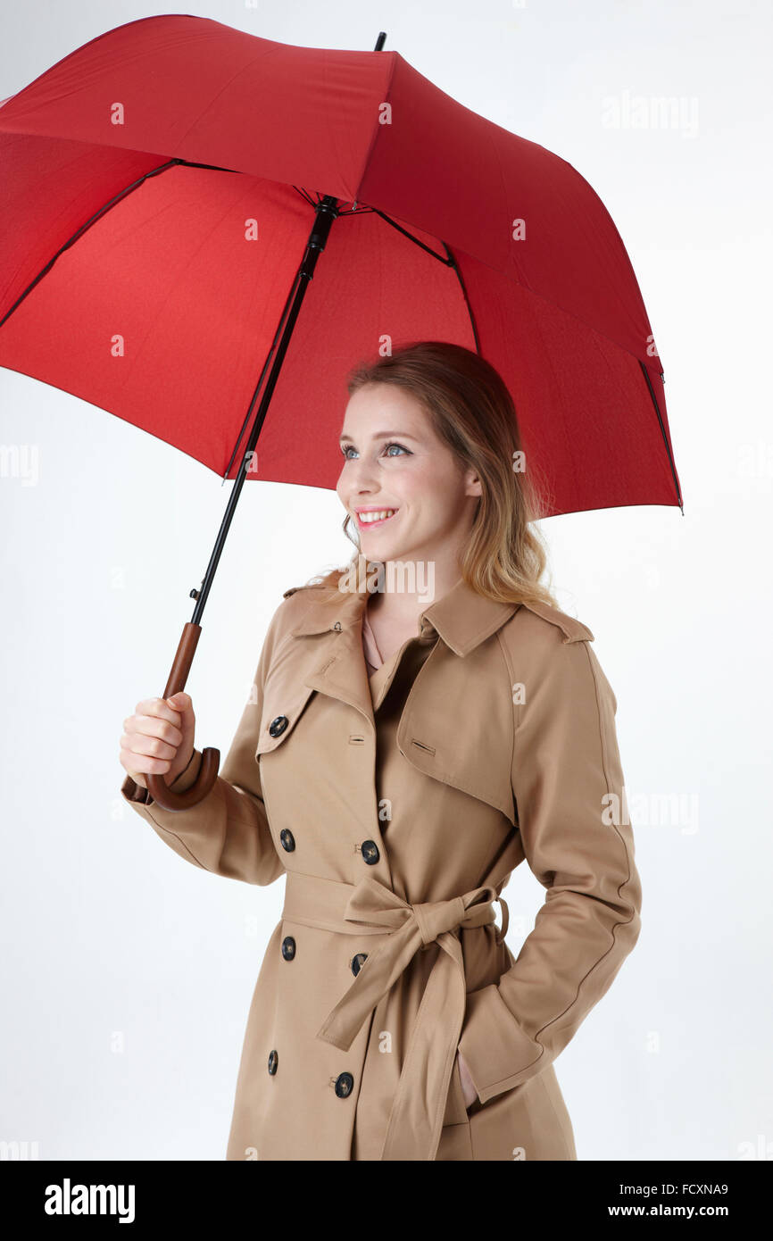 Jungen lächelnde Frau mit roten Regenschirm und legte eine Hand in der Tasche nachschlagen trenchcoat Stockfoto
