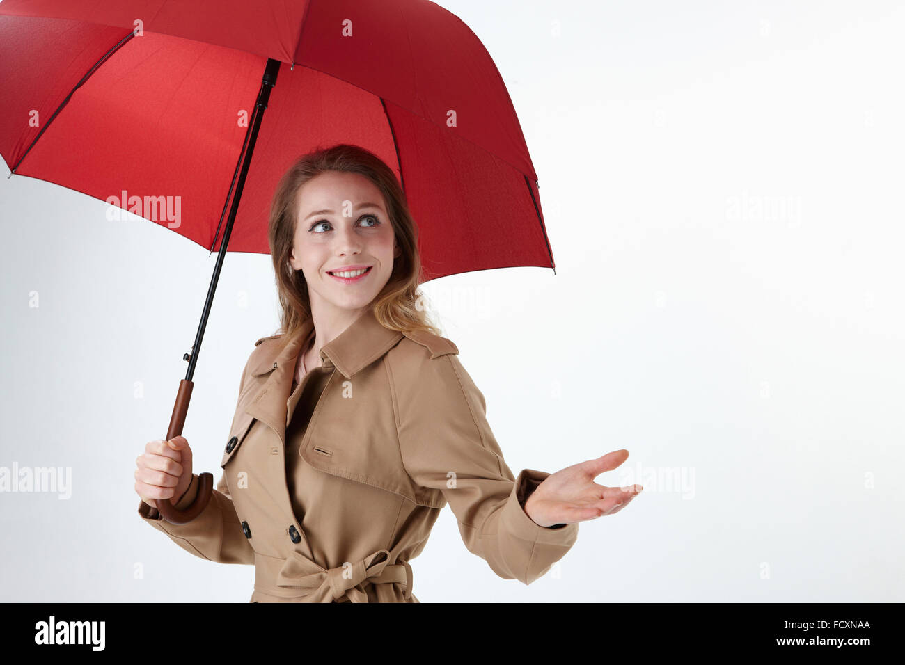 Porträt des jungen lächelnde Frau mit roten Regenschirm und Trenchcoat im Besitz einer Hand nach oben Stockfoto