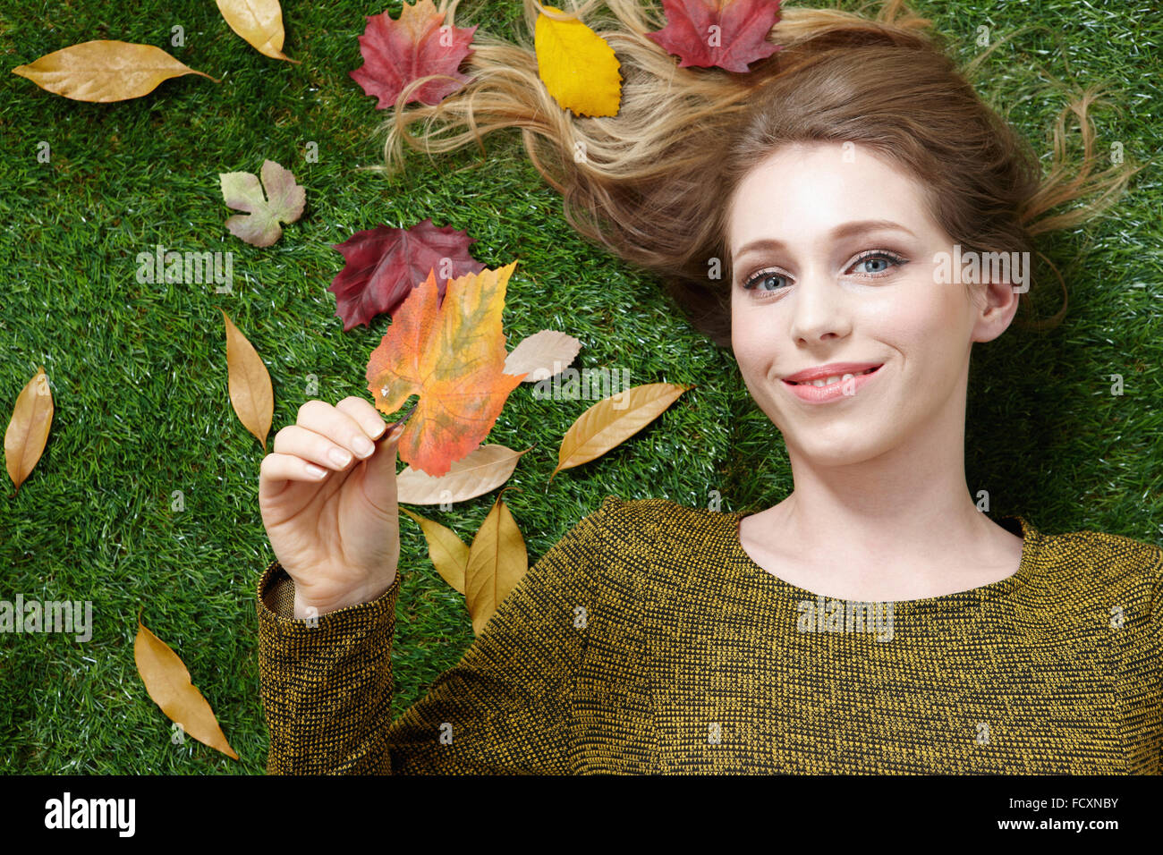 Porträt des jungen lächelnd lächelnde Frau mit langen Haaren auf dem Rasen mit Laub liegend Stockfoto