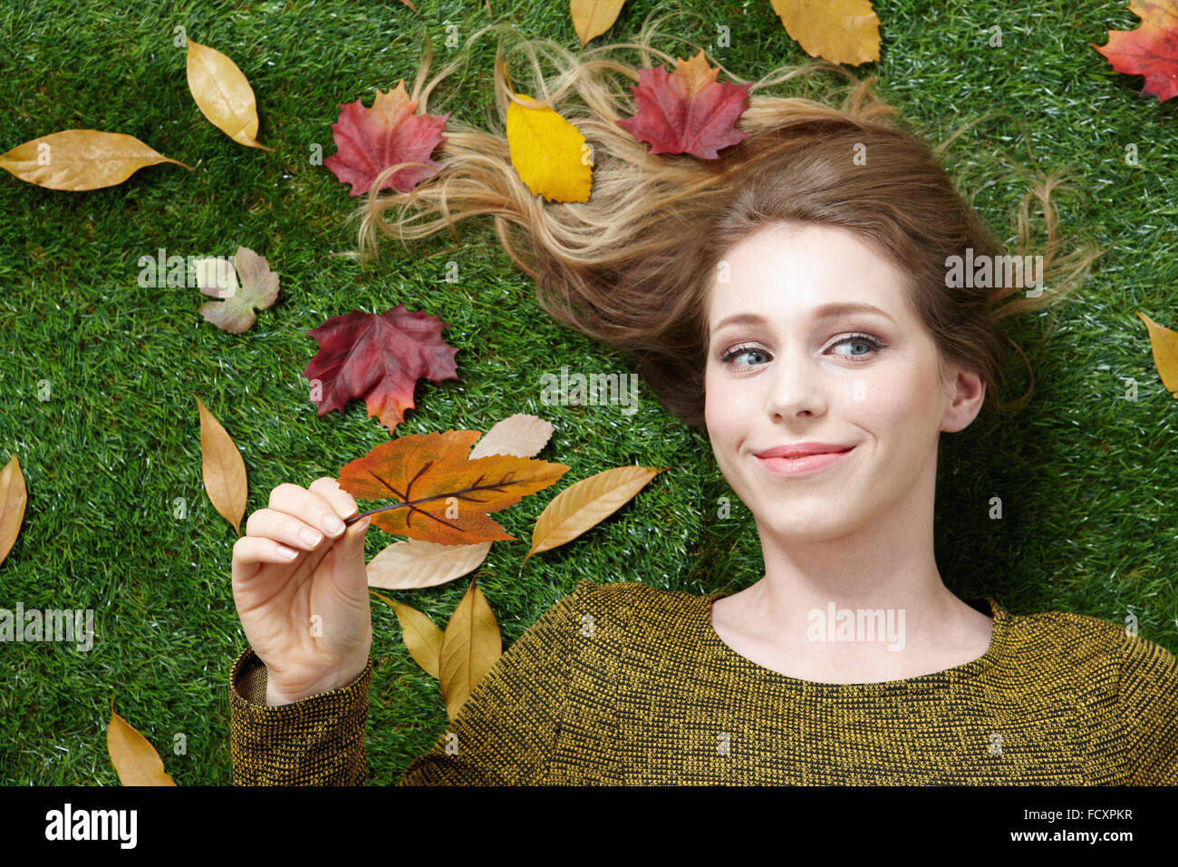 Porträt des jungen lächelnde Frau mit langen Haaren auf dem Rasen mit Laub liegend Stockfoto
