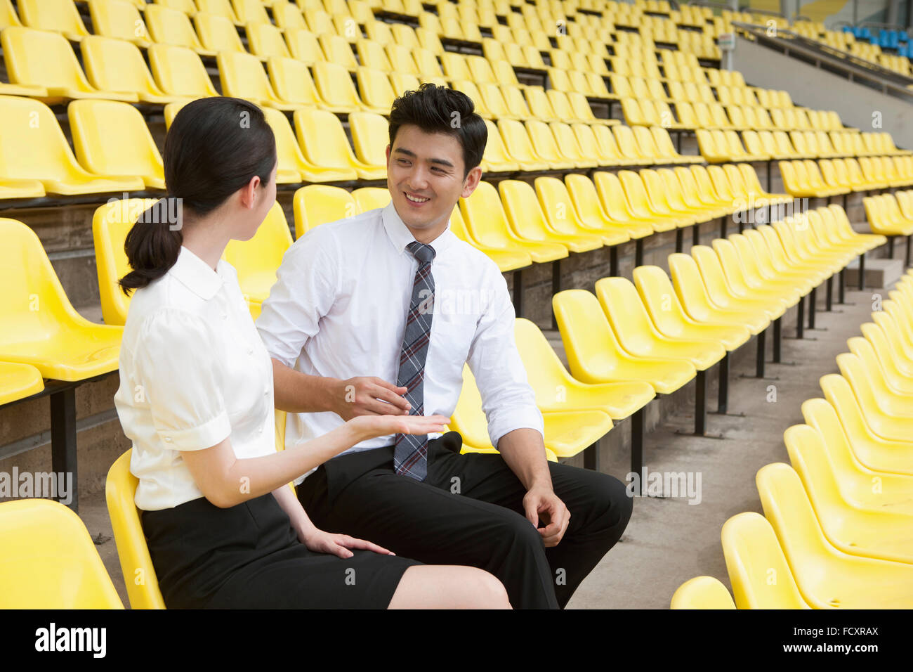 Lächelnder Mann und Frau in Anzügen auf Stadionsitze sitzen und reden von Angesicht zu Angesicht Stockfoto