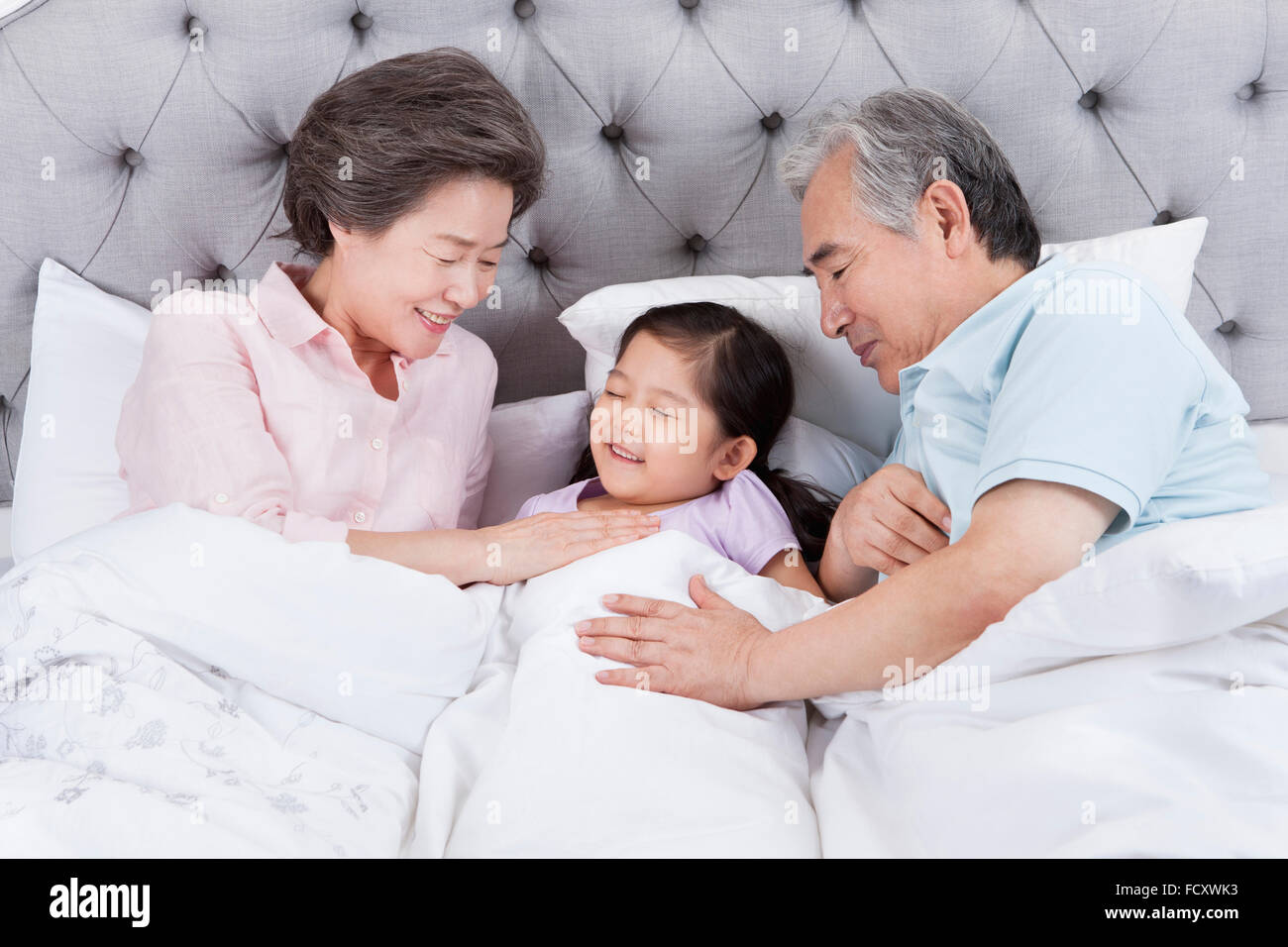 Liebevolle Großeltern setzen ihre Enkelin im Bett schlafen Stockfoto