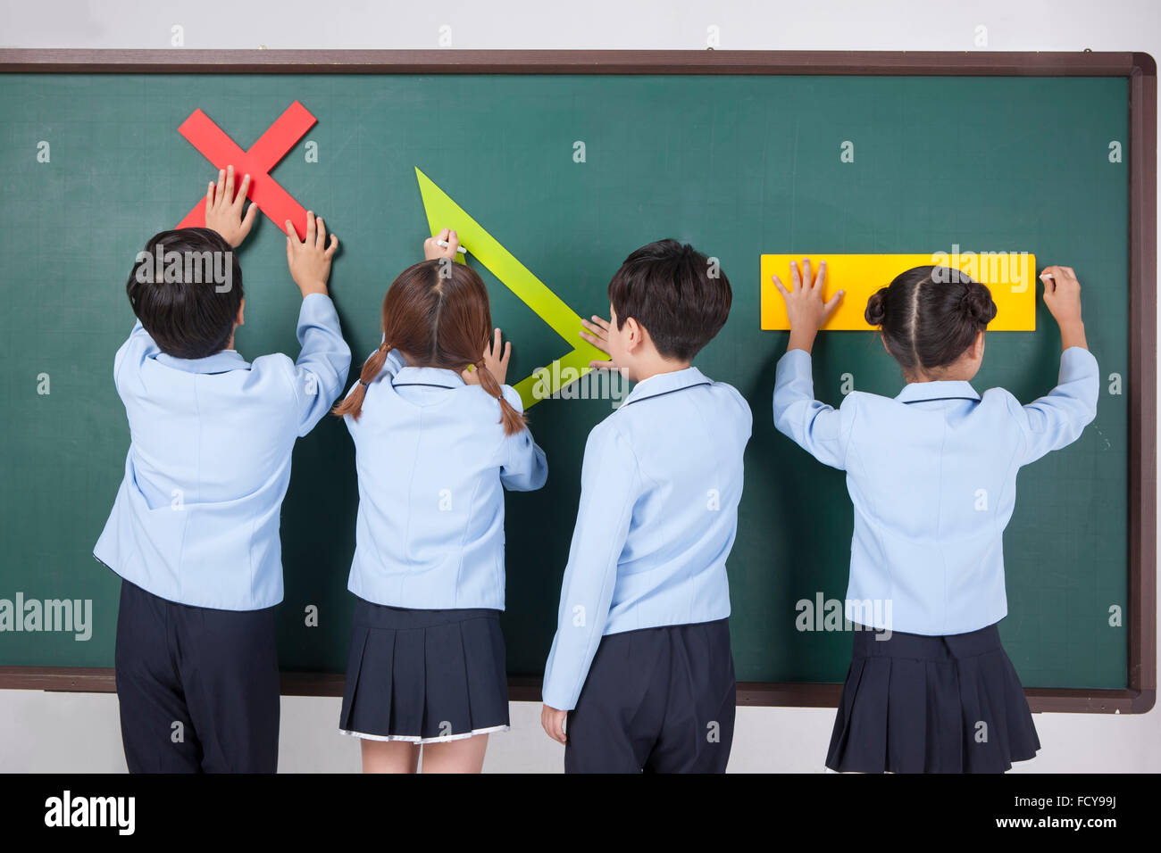 Vier Grundschüler ein Objekt im Zusammenhang mit Mathematik jedes und setzen sie an die Tafel zu halten Stockfoto