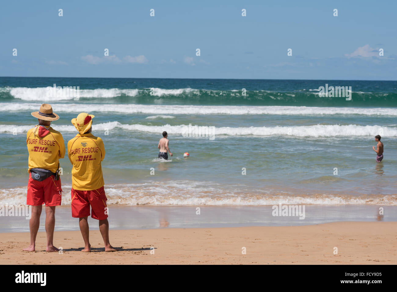 Rettungsschwimmer am Manly Beach, Australien. Trotz den Warnzeichen für starke Brandung spielen zwei Männer in der Brandung am Nationalfeiertag Australia Day sah vorsichtig zwei Rettungsschwimmer Stockfoto