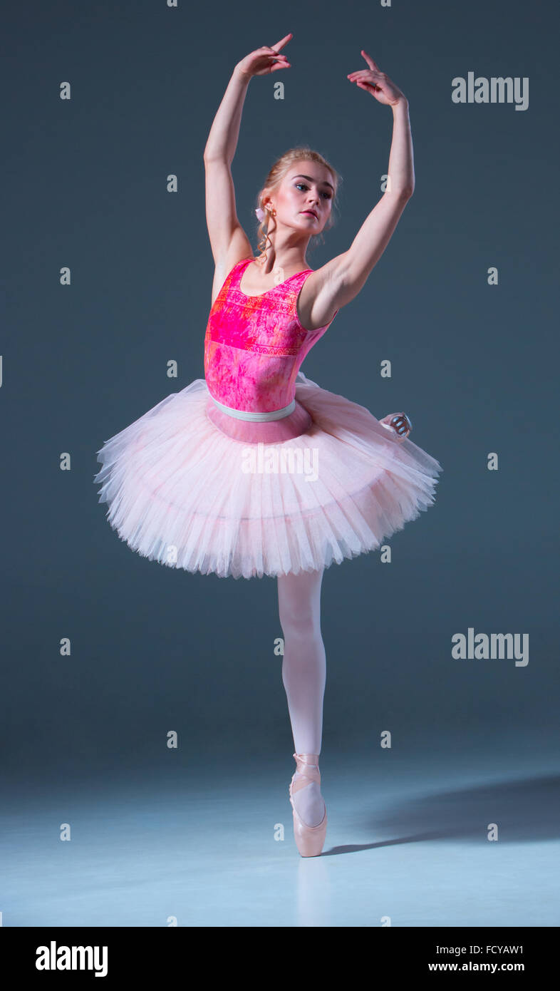 Porträt der Ballerina im Ballett posieren auf einem grauen Hintergrund. Ballerina ist rosa Tutu und Pointe Schuhe tragen. Stockfoto